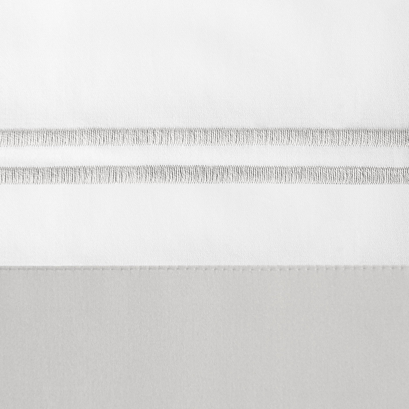 Close-up of fringe trim detail on white and silver-grey cotton pillowcase border.
