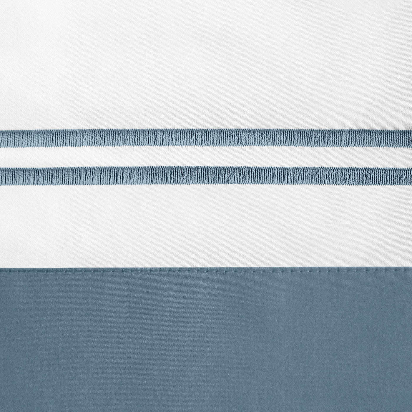 Close-up of slate blue embroidered stripe detail on white and blue cotton pillow sham.
