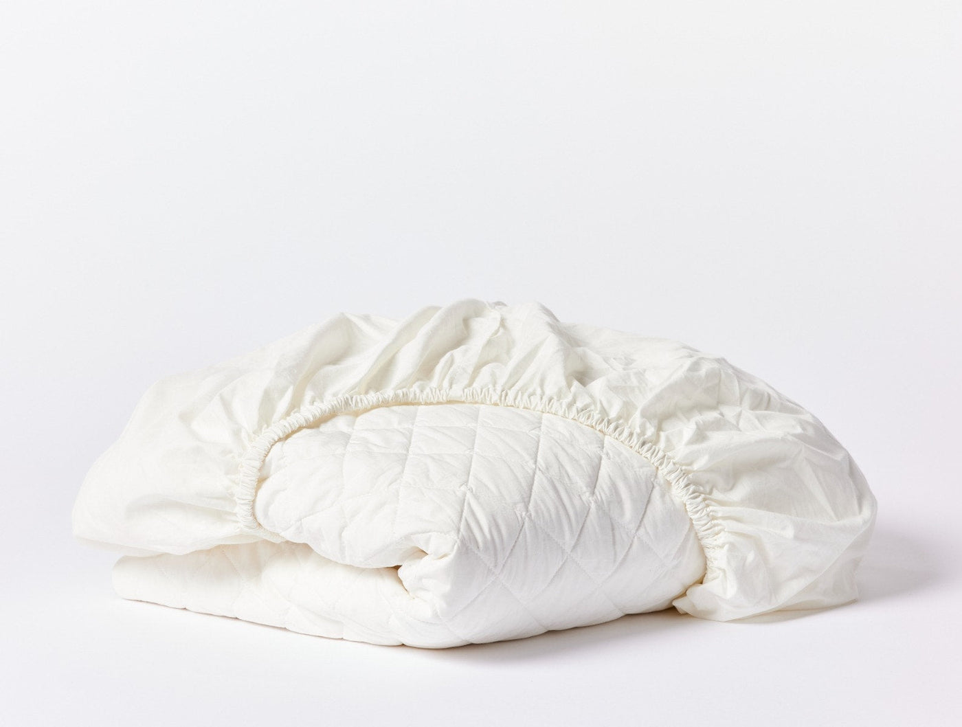 Coyuchi Cotton Mattress Pad in ivory, folded to show quilted top and elasticized edges.