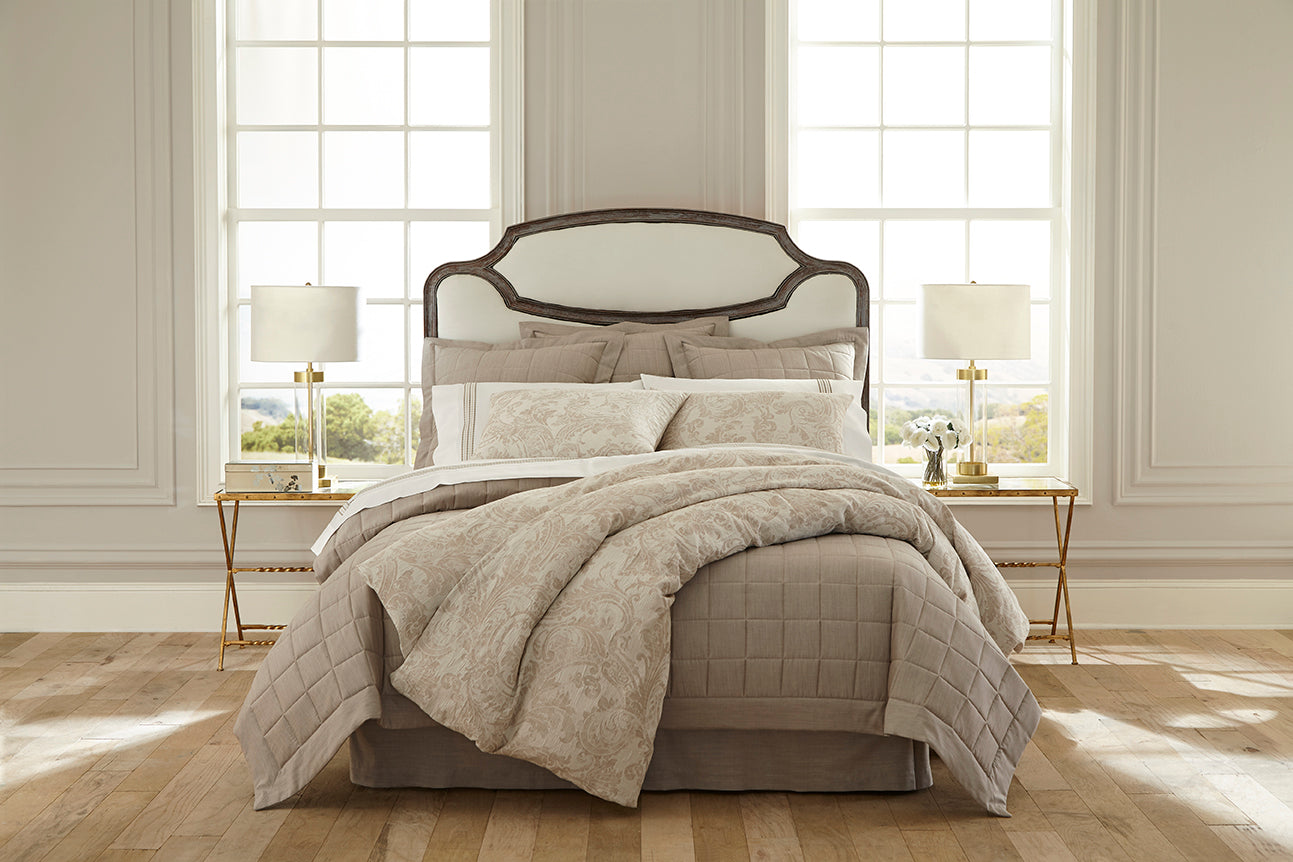 Champagne quilted bedding with textured floral throw styled on a bed in a bright bedroom.