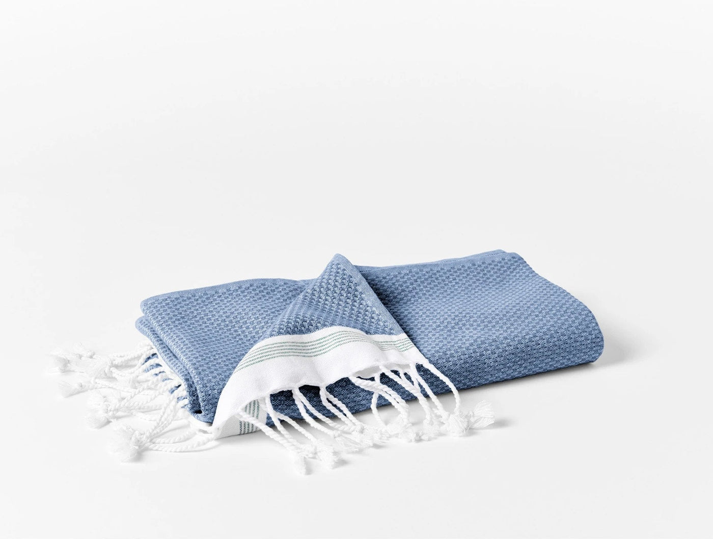 Coyuchi Mediterranean wash cloth in slate blue, folded with white fringe detail visible.