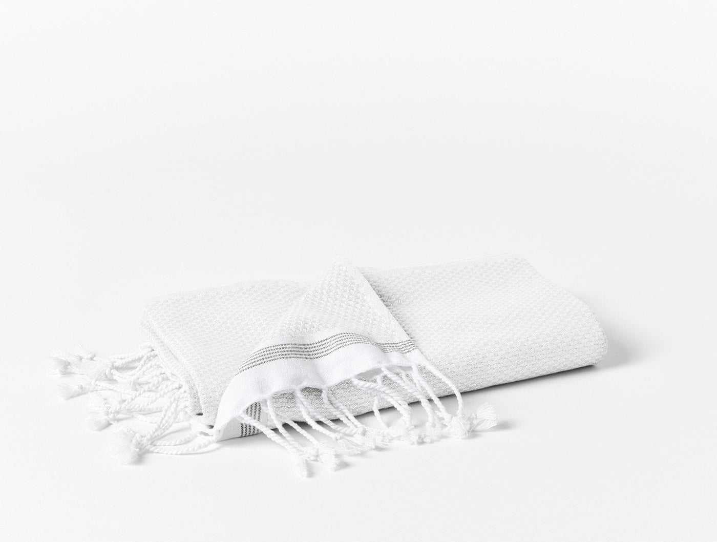 Folded white Coyuchi Mediterranean beach towel showing knotted fringe detail against white background.