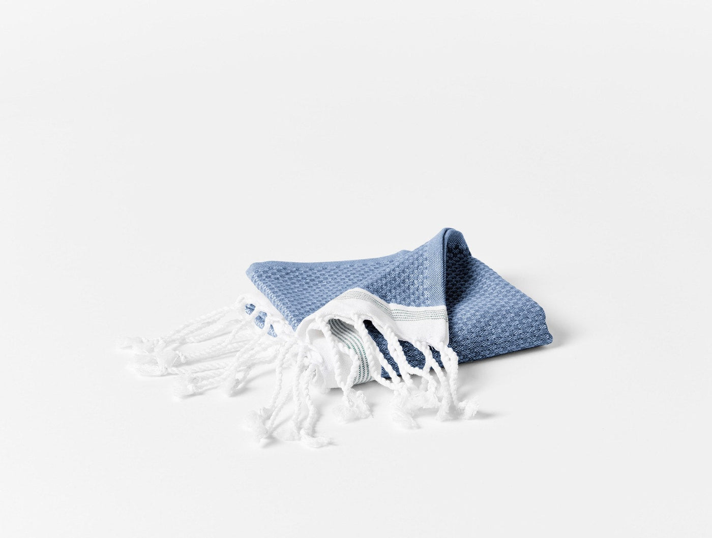 Close-up of folded Coyuchi Mediterranean bath towel in blue with white fringe detail.