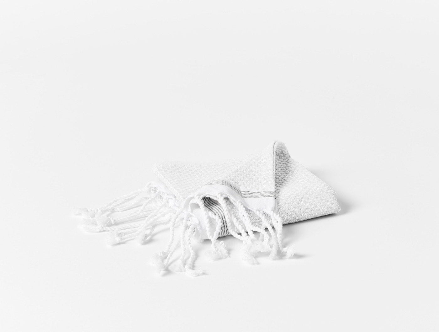 Coyuchi Mediterranean wash cloth folded with knotted fringe detail, white waffle weave texture.