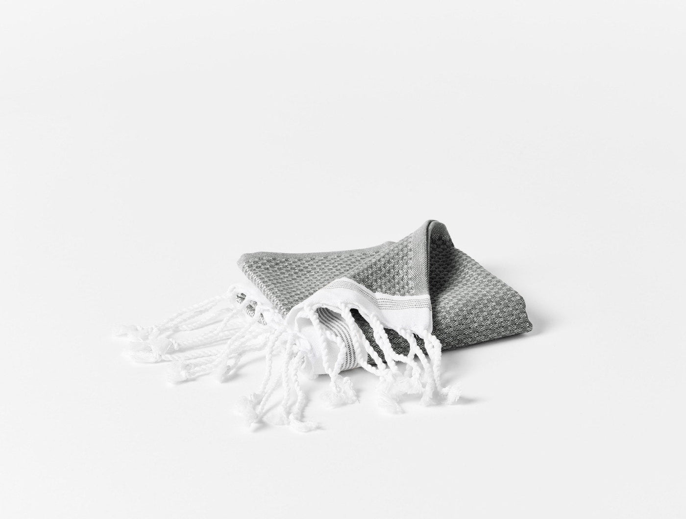 Folded grey waffle-weave beach towel with white knotted fringe, on white background.