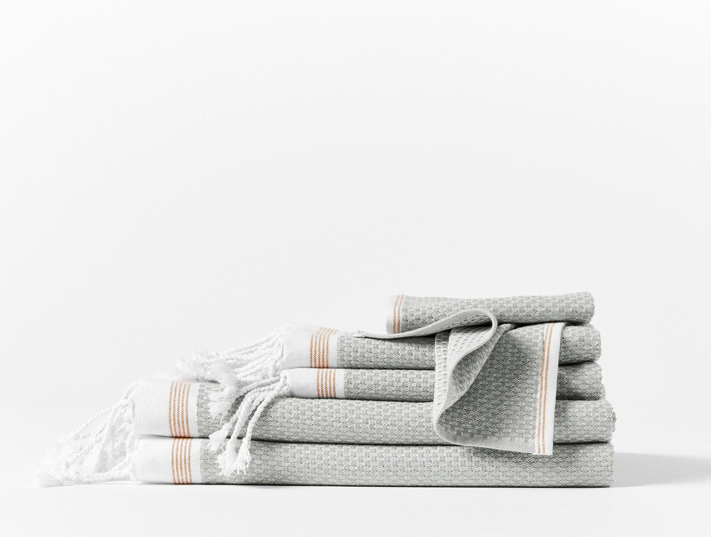 Sage waffle-weave towel set with terracotta stripe trim and white fringe, stacked on white surface.