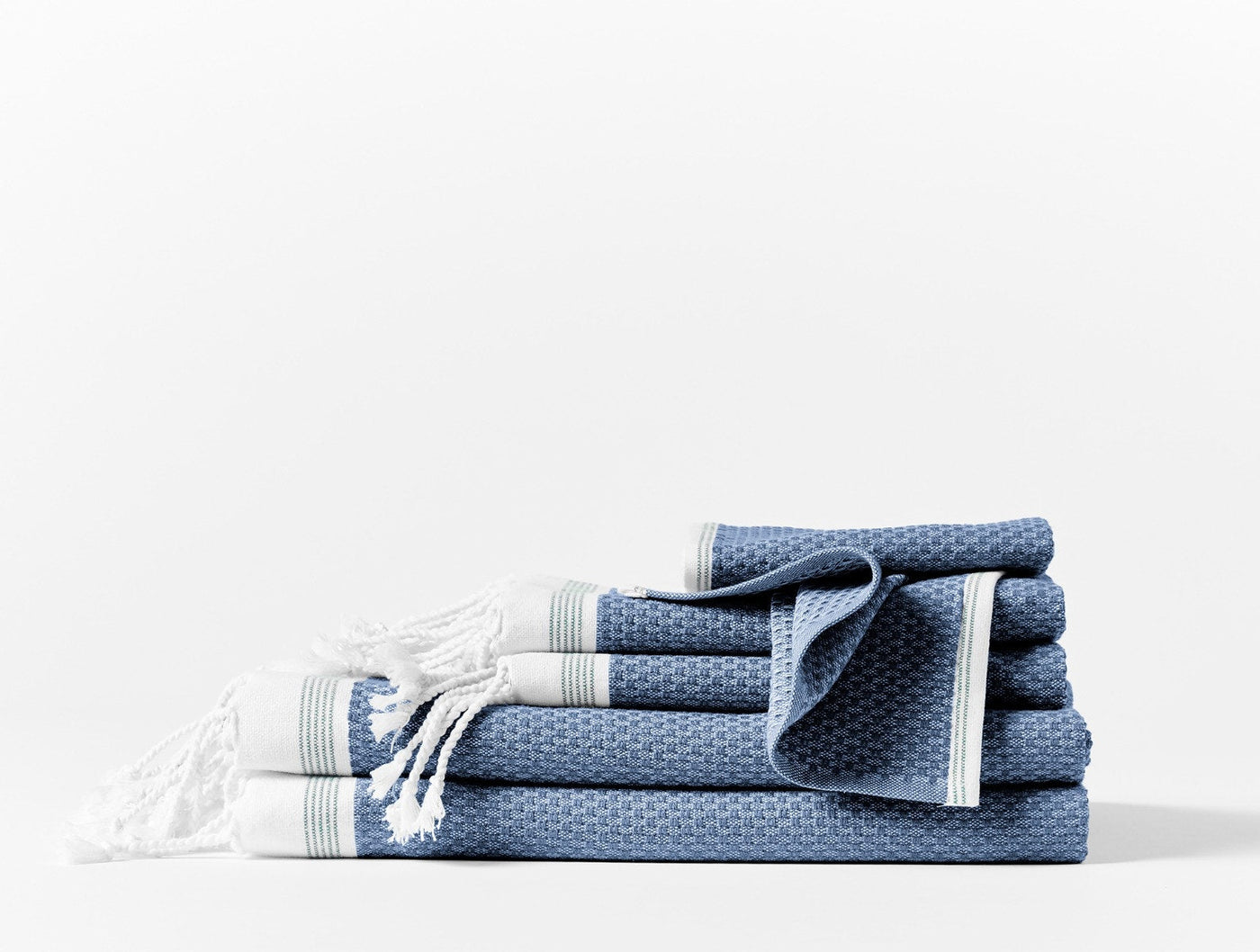 Stacked indigo waffle-weave bath towels with white fringe and stripe trim detail.