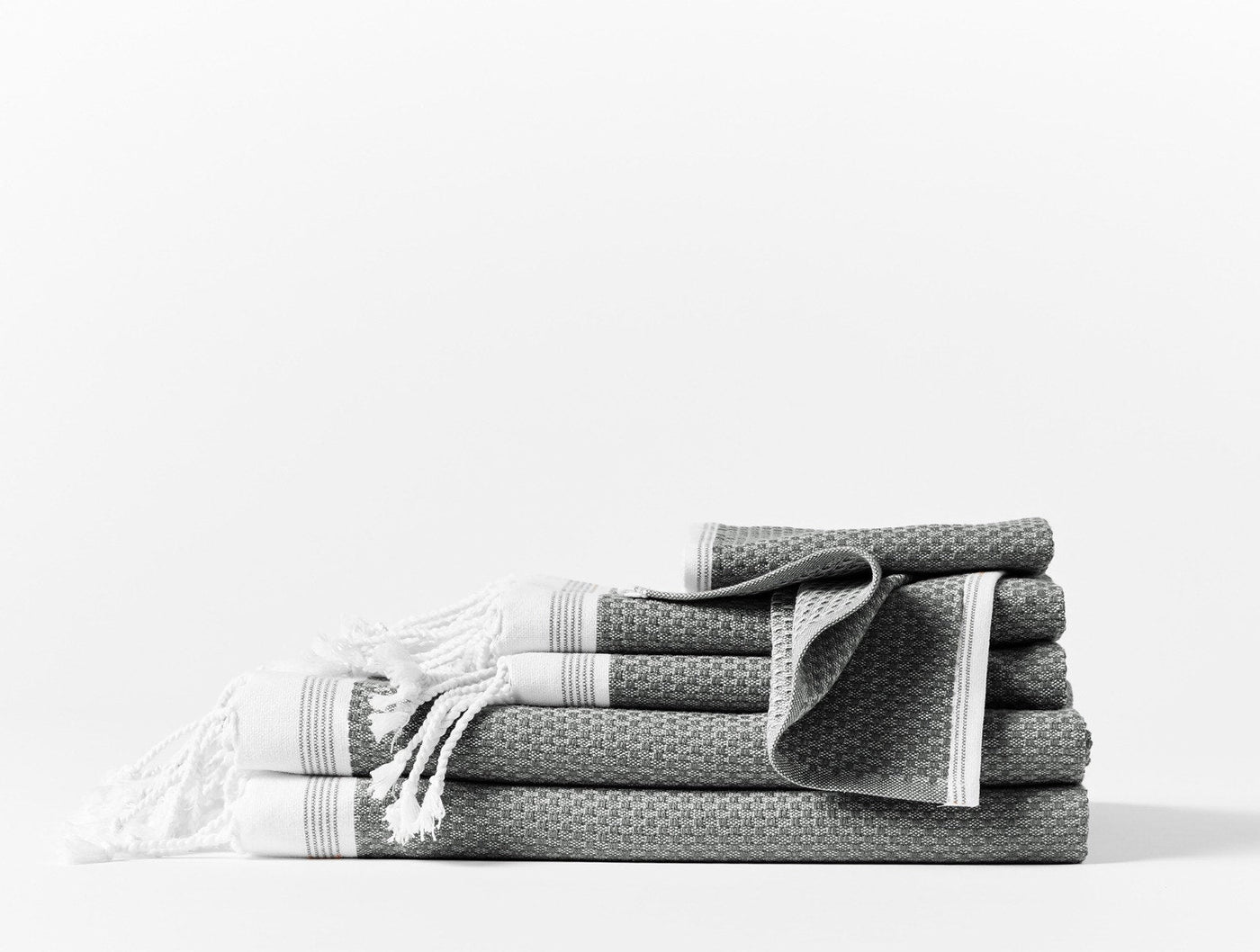 Slate grey waffle-weave towel set with white fringe and stripe trim, stacked and folded.