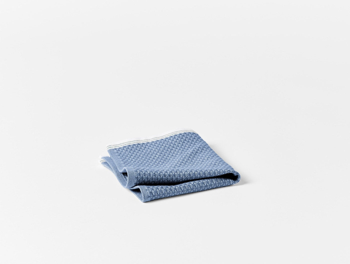 Close-up of folded slate blue Coyuchi Mediterranean beach towel showing waffle weave texture.