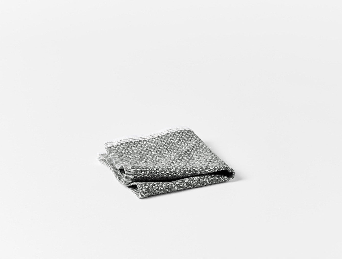Close-up of folded grey Coyuchi Mediterranean beach towel showing textured weave and white border trim.
