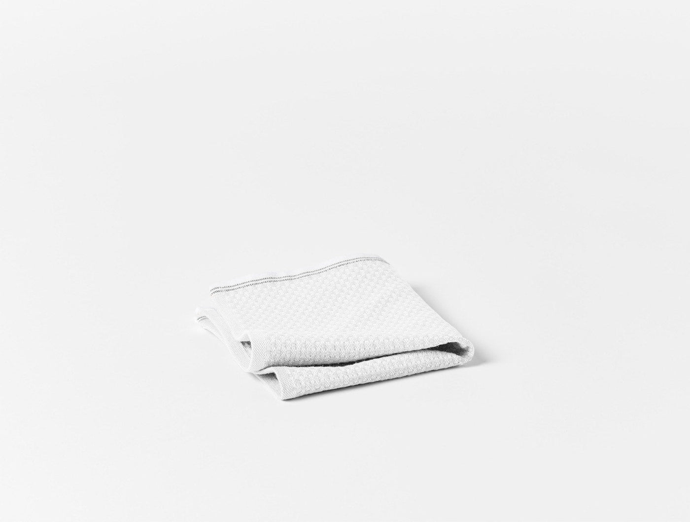 Close-up of folded white waffle-weave washcloth with subtle gray border trim.