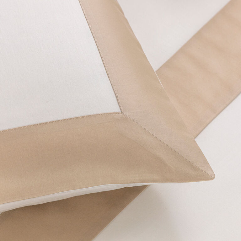 Close-up of Frette’s Bold | Sleeping Sham in white cotton sateen with a beige border, shown on a matching beige sheet, highlighting its luxurious texture and classic design.