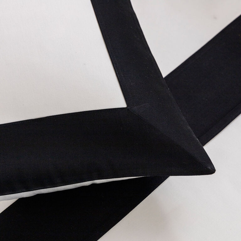 Close-up of the Frette Bold | Sleeping Sham in cotton sateen, showing a wide black border on white, set on a matching black-and-white surface.