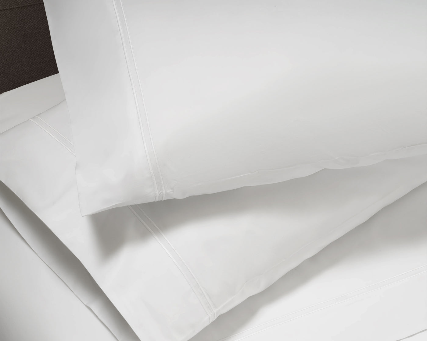 Close-up of white cotton pillowcase with triple-row embroidered hem detail.