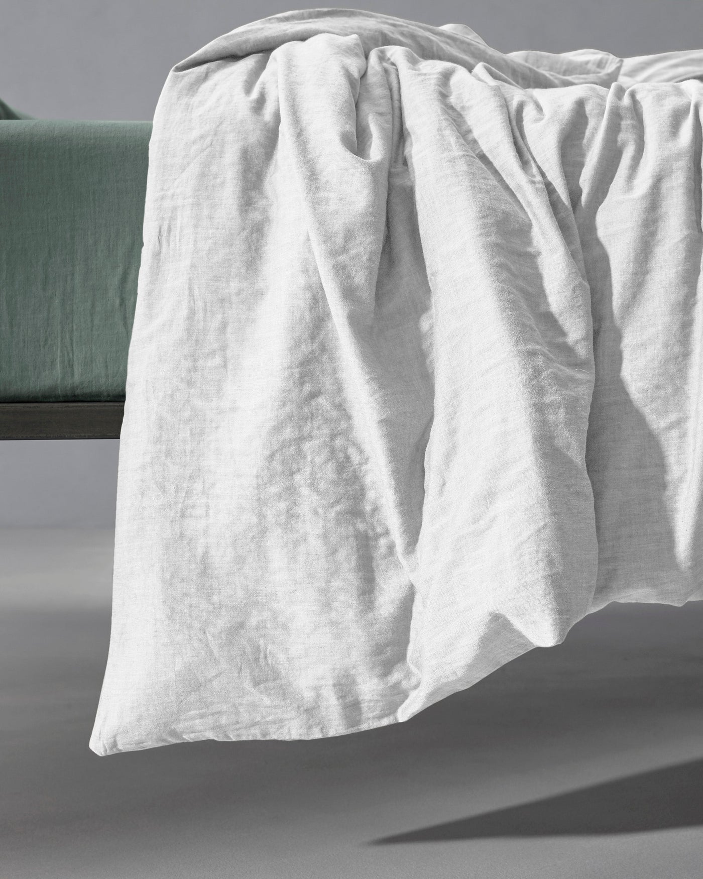 Society Limonta Miro plain duvet cover in white washed linen draped over a sage green bed frame.