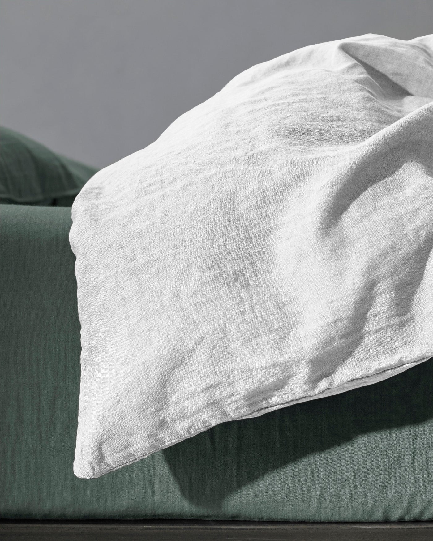 Close-up of white washed linen pillowcase resting against a forest green duvet cover.