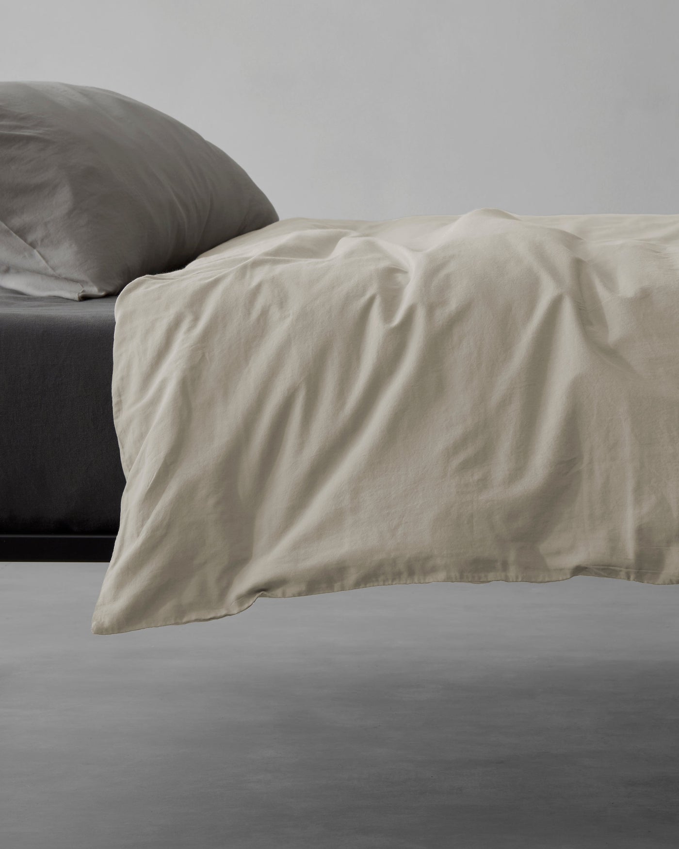 Oatmeal linen duvet cover draped over the foot of a bed, showing natural texture and soft drape.