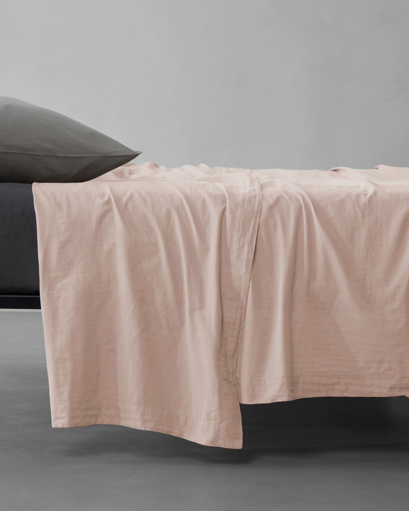 Blush flat sheet draped loosely over a bed with charcoal pillowcase visible.