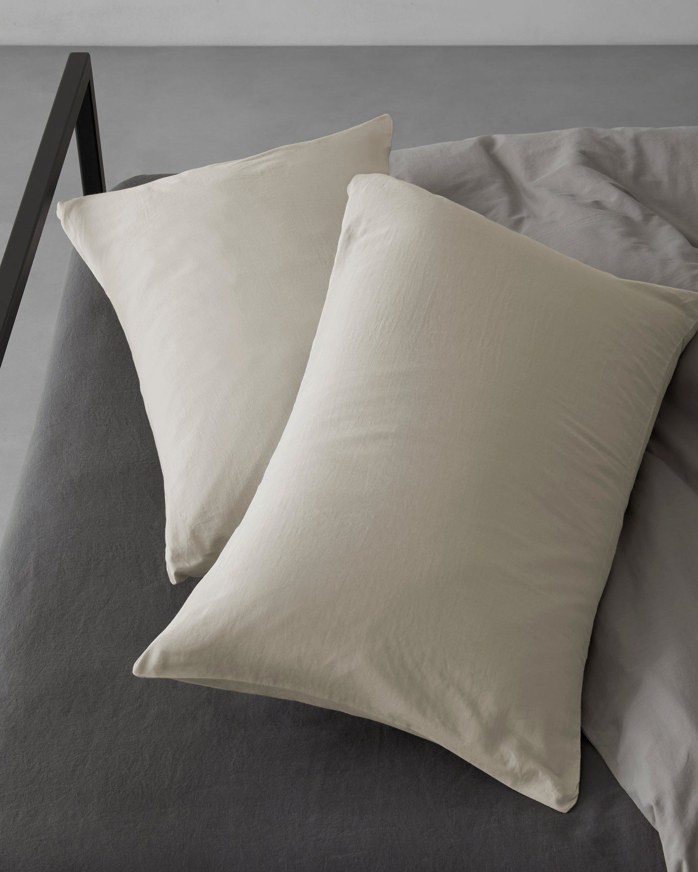 Two Society Limonta Miro pillowcases in parchment, stacked on a charcoal bed.