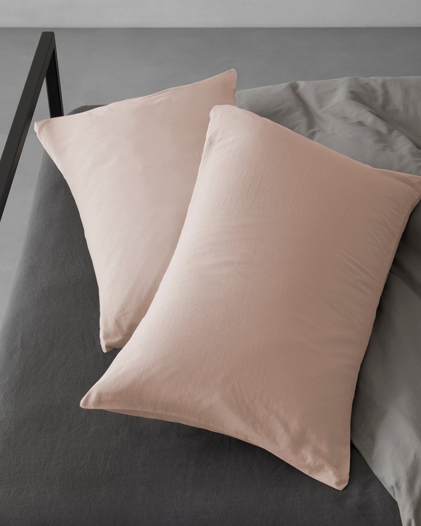 Two Society Limonta Miro pillowcases in blush, angled overhead view on charcoal bedding.
