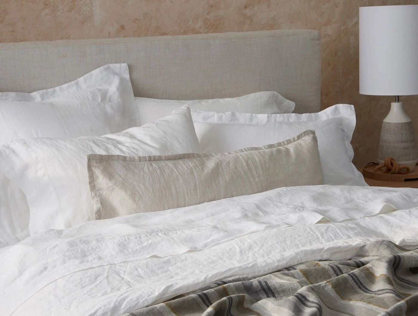 Close-up of a natural linen lumbar pillow styled among white bedding on a made bed.