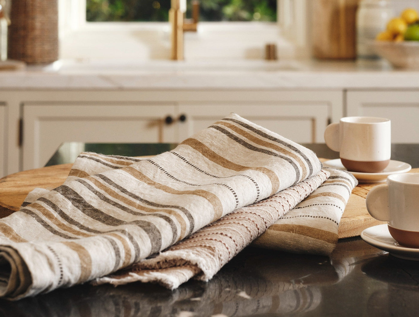 Coyuchi Mojave linen hand towels folded on wood board, tan and brown stripe detail.