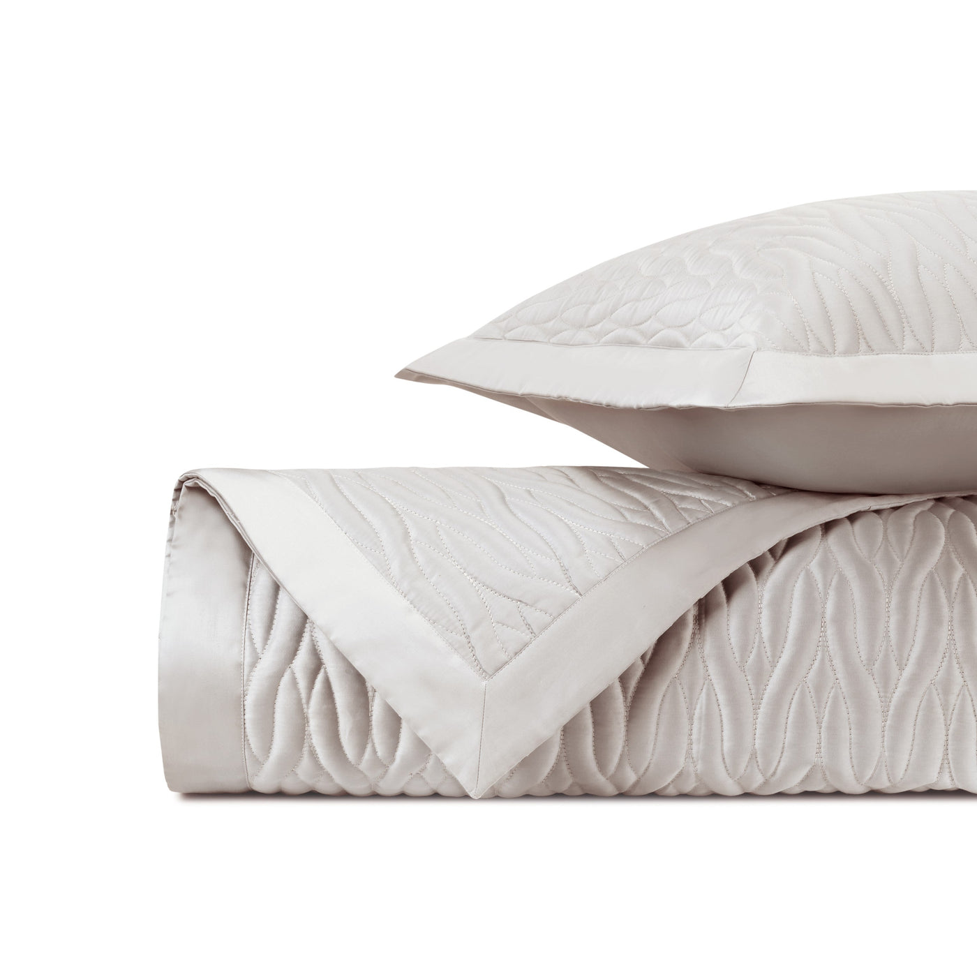 Close-up of ivory quilted texture with satin border on folded coverlet and sham.