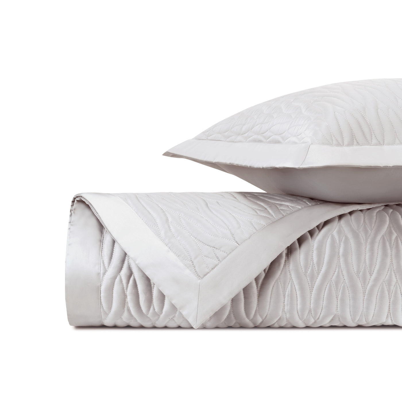 Close-up of ivory quilted coverlet with wave-pattern stitching and satin border trim.