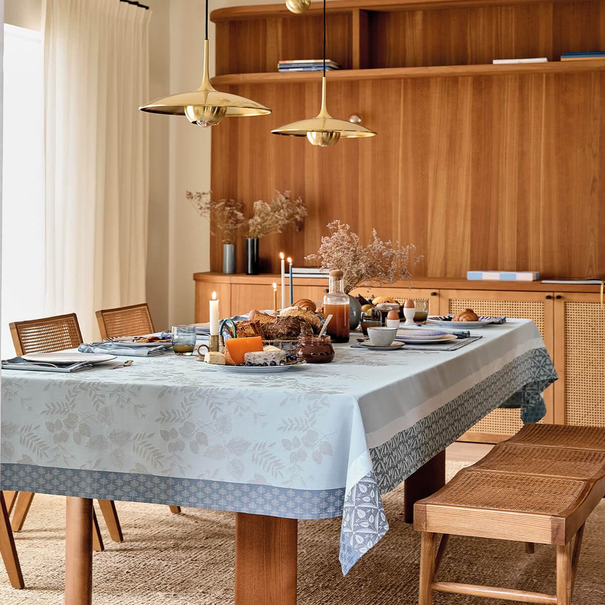 Le Jacquard Français Manor Lane tablecloth in Blue, styled on a set dining table in a warm wood room.