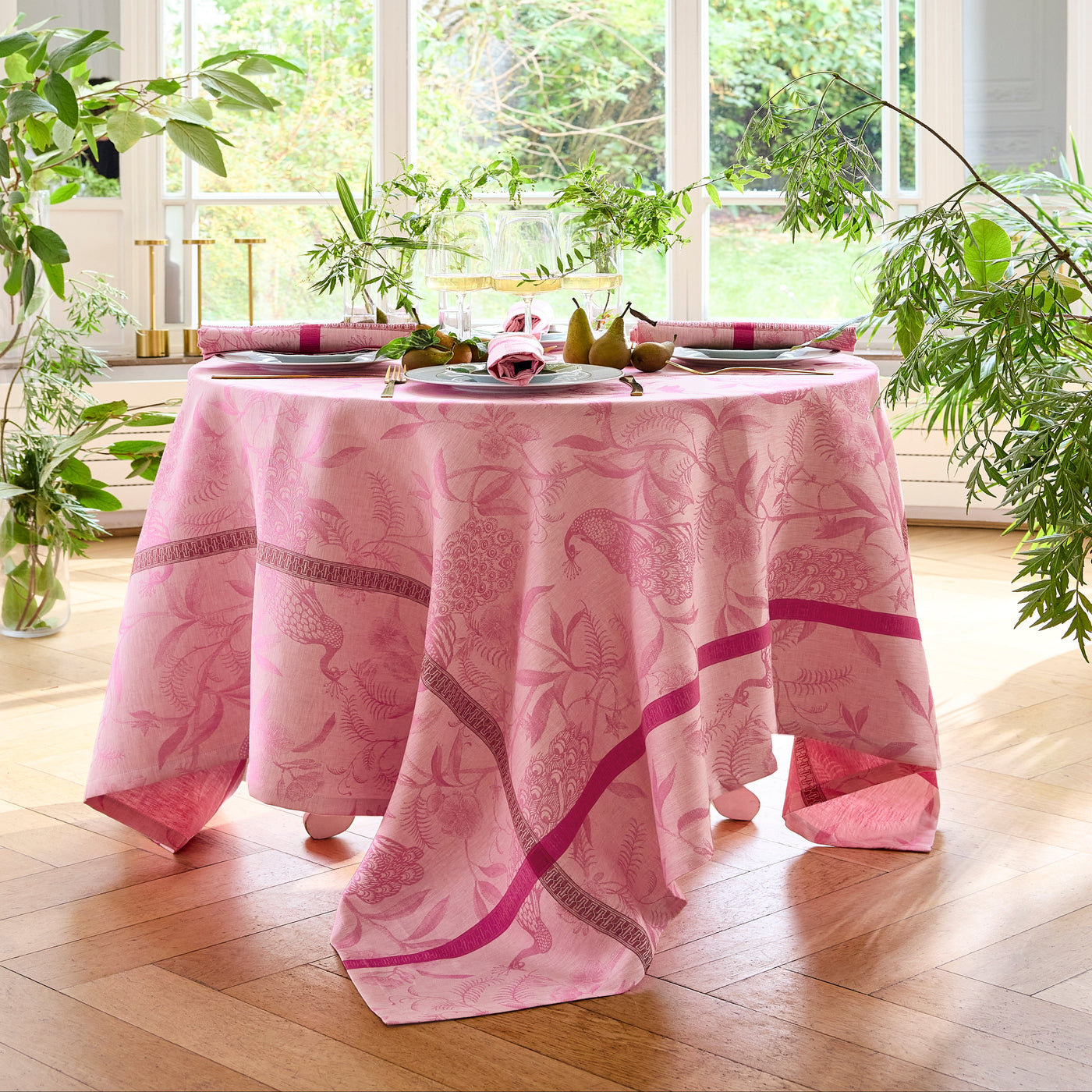 Rose pink jacquard tablecloth draped over a round dining table with botanical motifs.