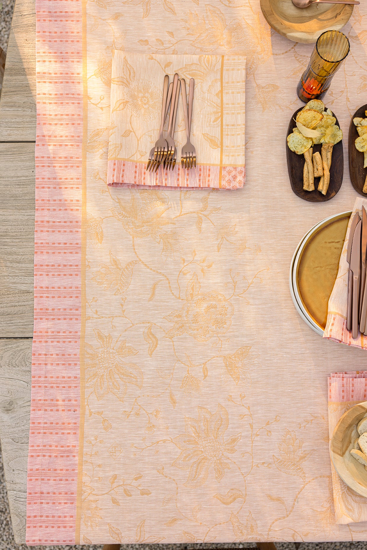Overhead view of blush linen tablecloth with golden floral jacquard pattern and coral striped border.