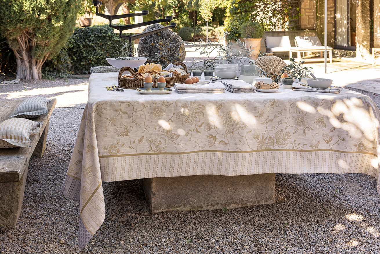 Stone terrace table styled with an ivory and gold jacquard tablecloth in dappled sunlight.