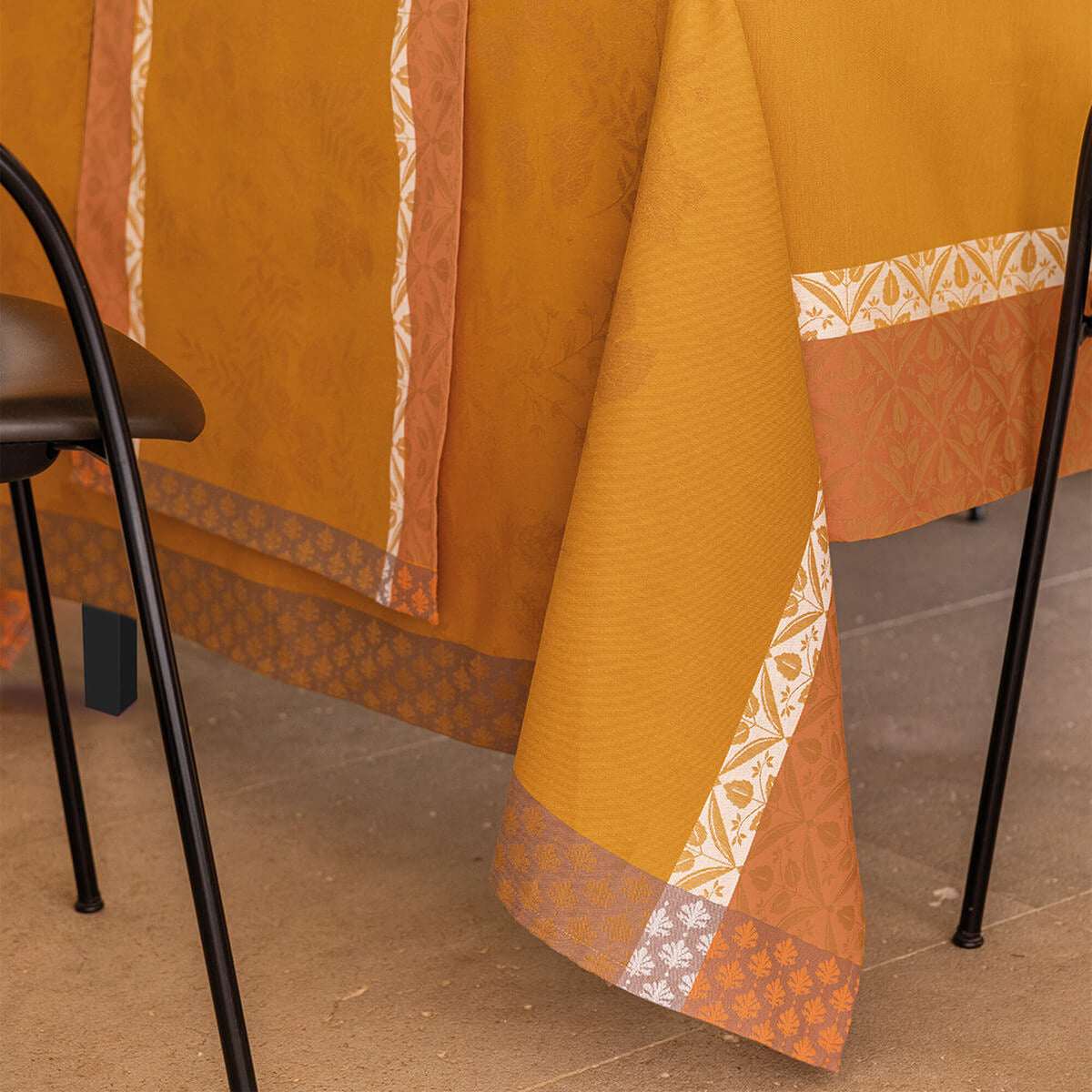 Le Jacquard Français Manor Lane tablecloth in Orange, draped over table showing jacquard border detail.