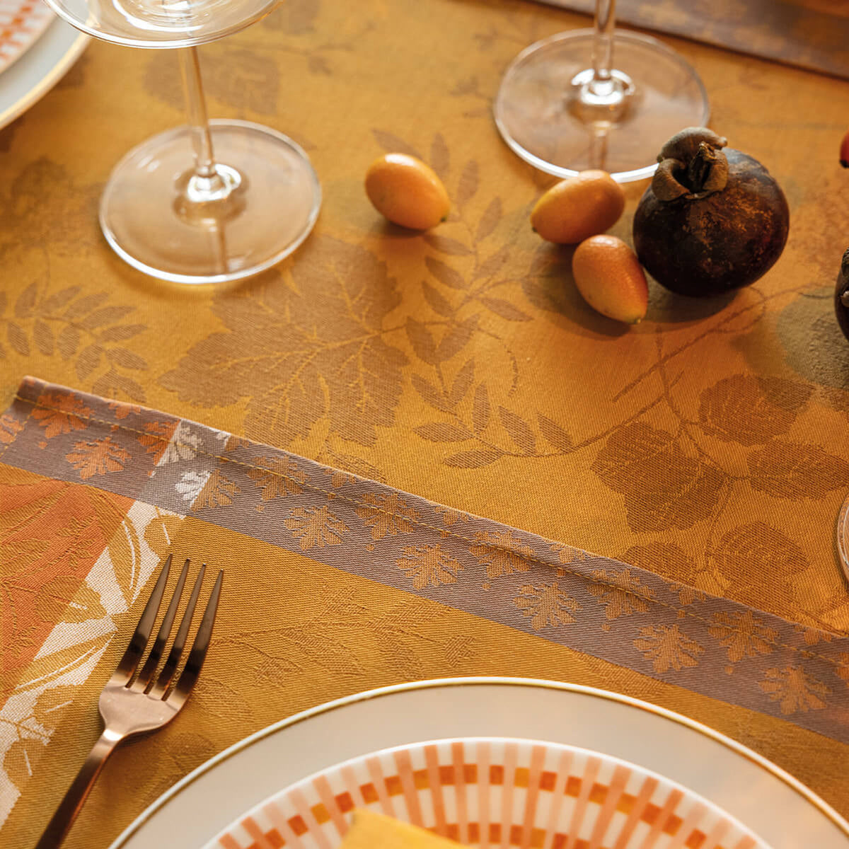 Close-up of Le Jacquard Français Manor Lane tablecloth in Orange, leaf jacquard weave with autumn table setting.