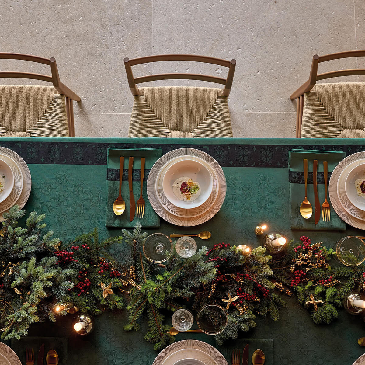 Overhead view of Green Le Jacquard Français tablecloth styled with holiday garland, gold cutlery, and candles.