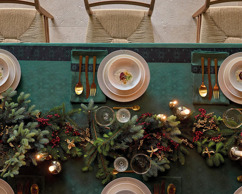Overhead view of Green Le Jacquard Français tablecloth styled with holiday garland, gold cutlery, and candles.