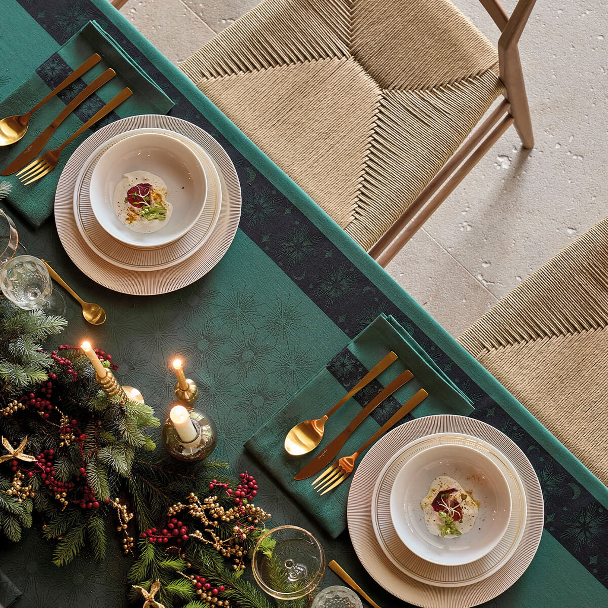 Green Sous les Étoiles tablecloth styled with holiday greenery, gold cutlery, and dinnerware overhead view.