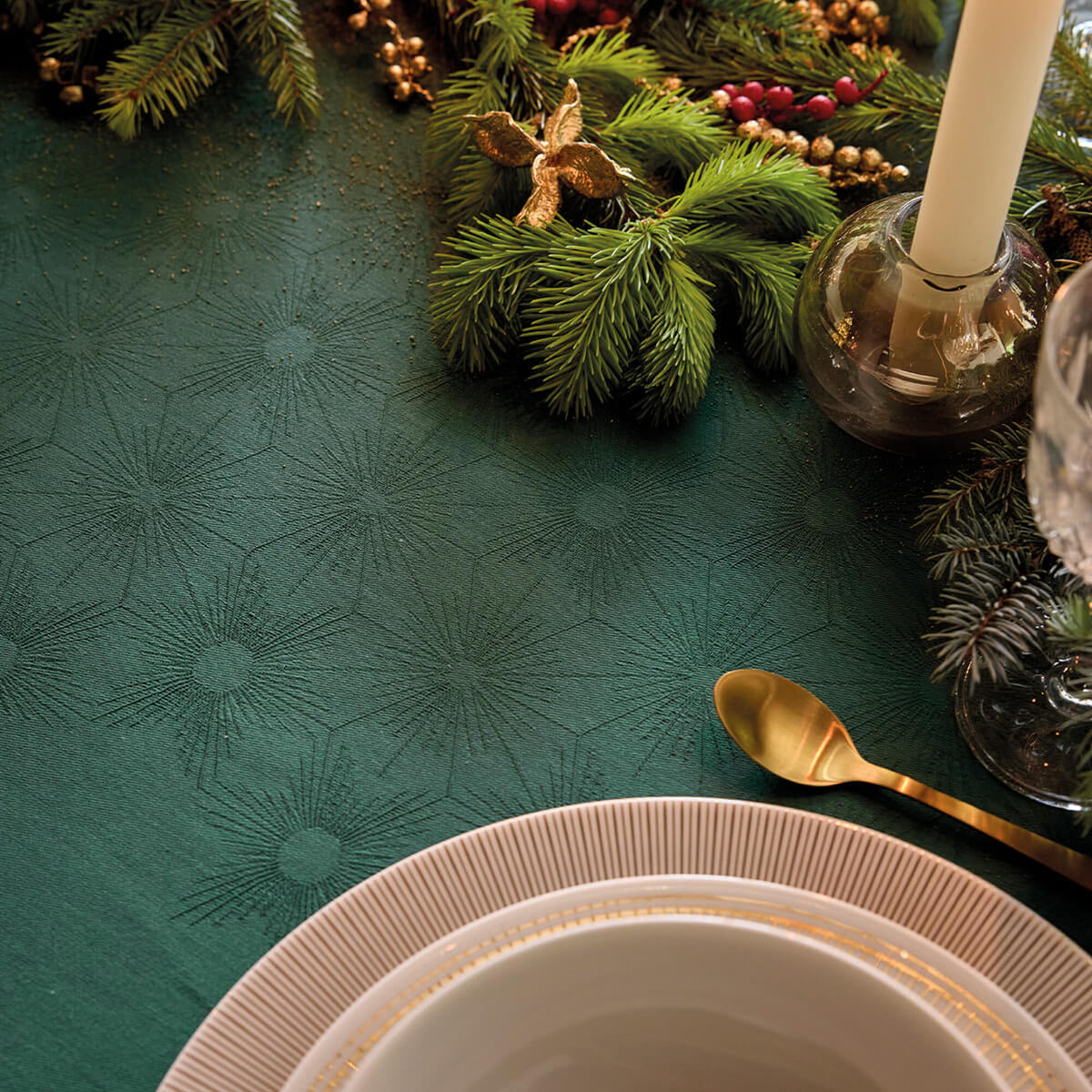 Green Sous les Étoiles tablecloth styled with holiday greenery, gold spoon, and stacked dinnerware.
