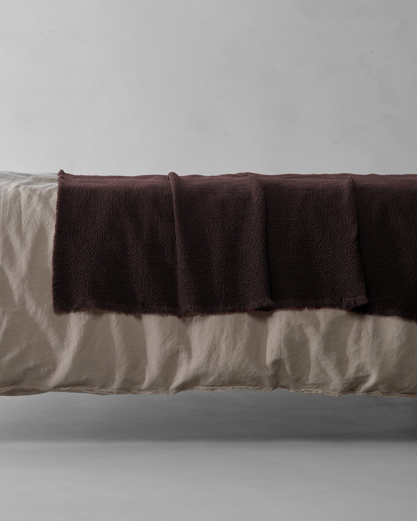 Society Limonta Nid blanket in deep plum draped across foot of linen bed.