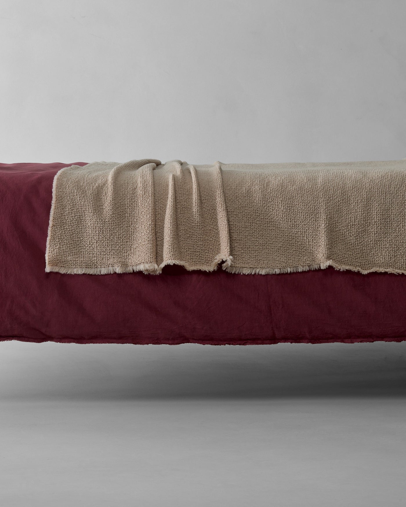 Fringe edge detail of Society Limonta Nid blanket in natural draped over burgundy bedding.
