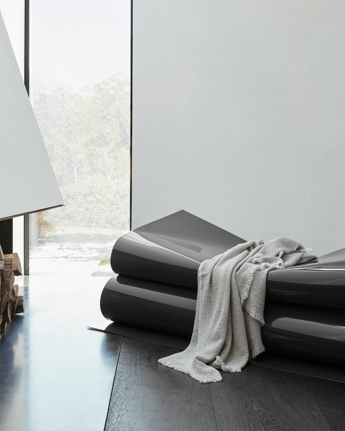 Ivory fringed blanket draped over a sculptural graphite bench in a minimalist interior.