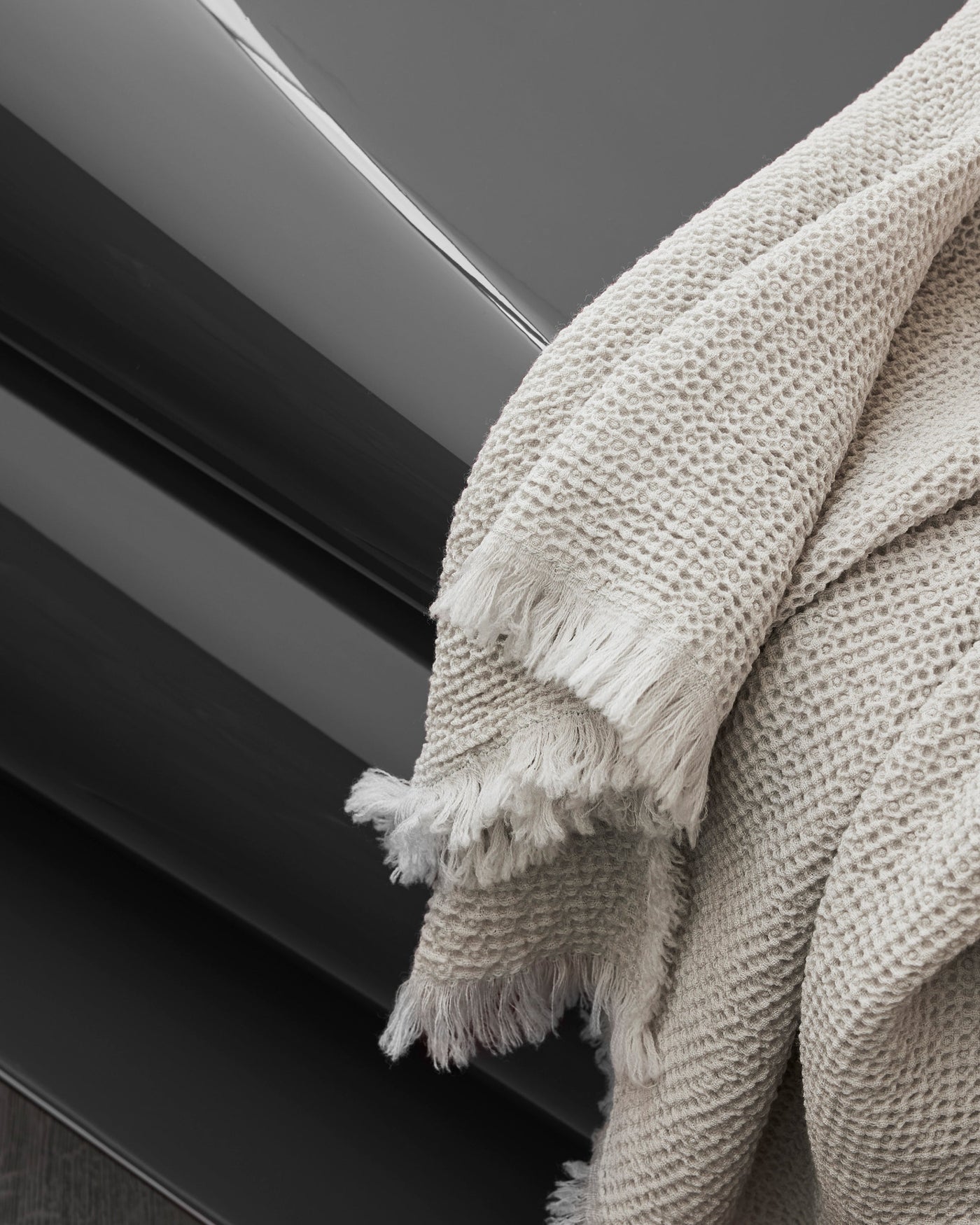 Society Limonta Nid ivory waffle-weave blanket with fringe trim draped over dark surface.