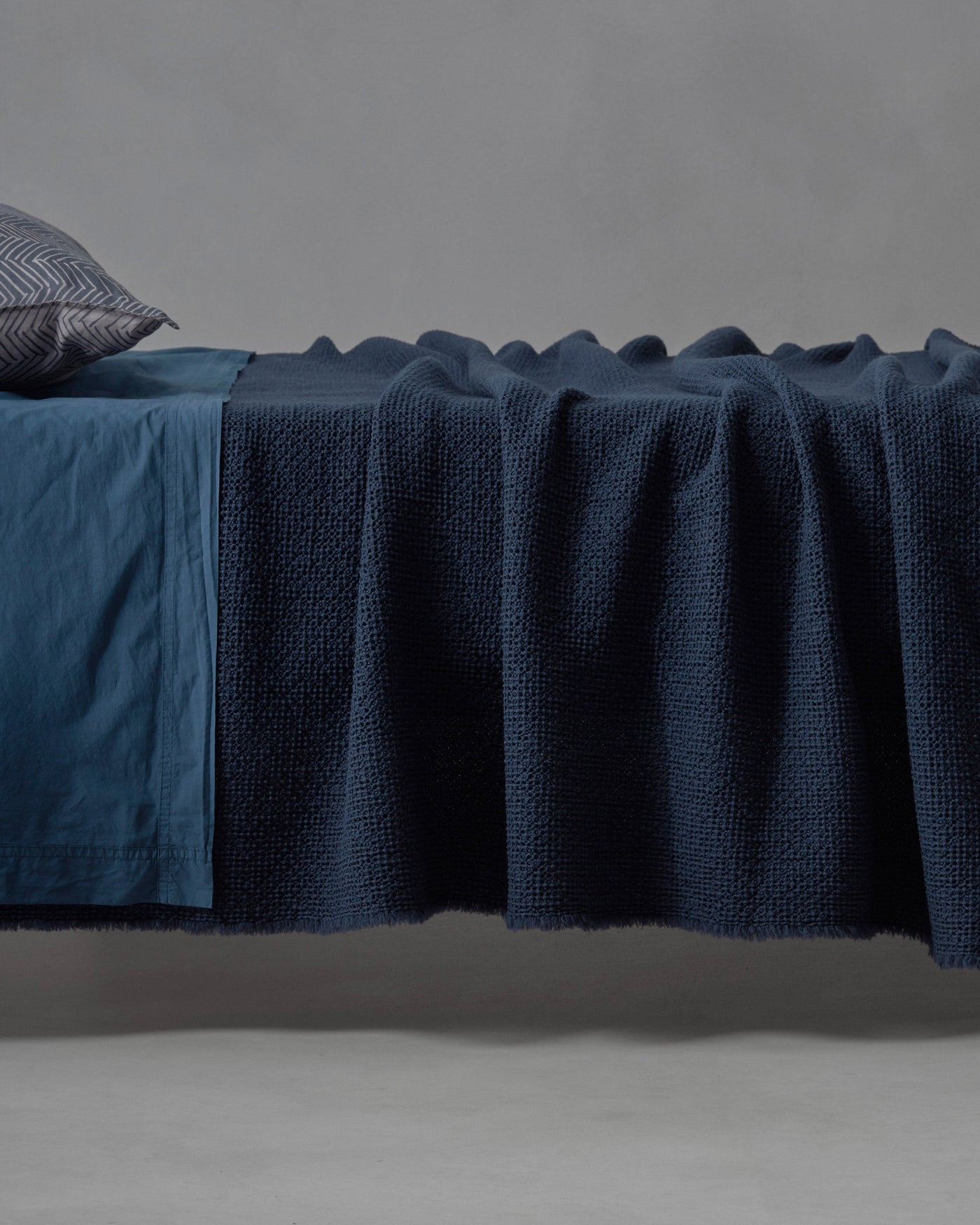 Close-up of Society Limonta Nid blanket in deep navy, waffle-knit texture draped over bed edge.