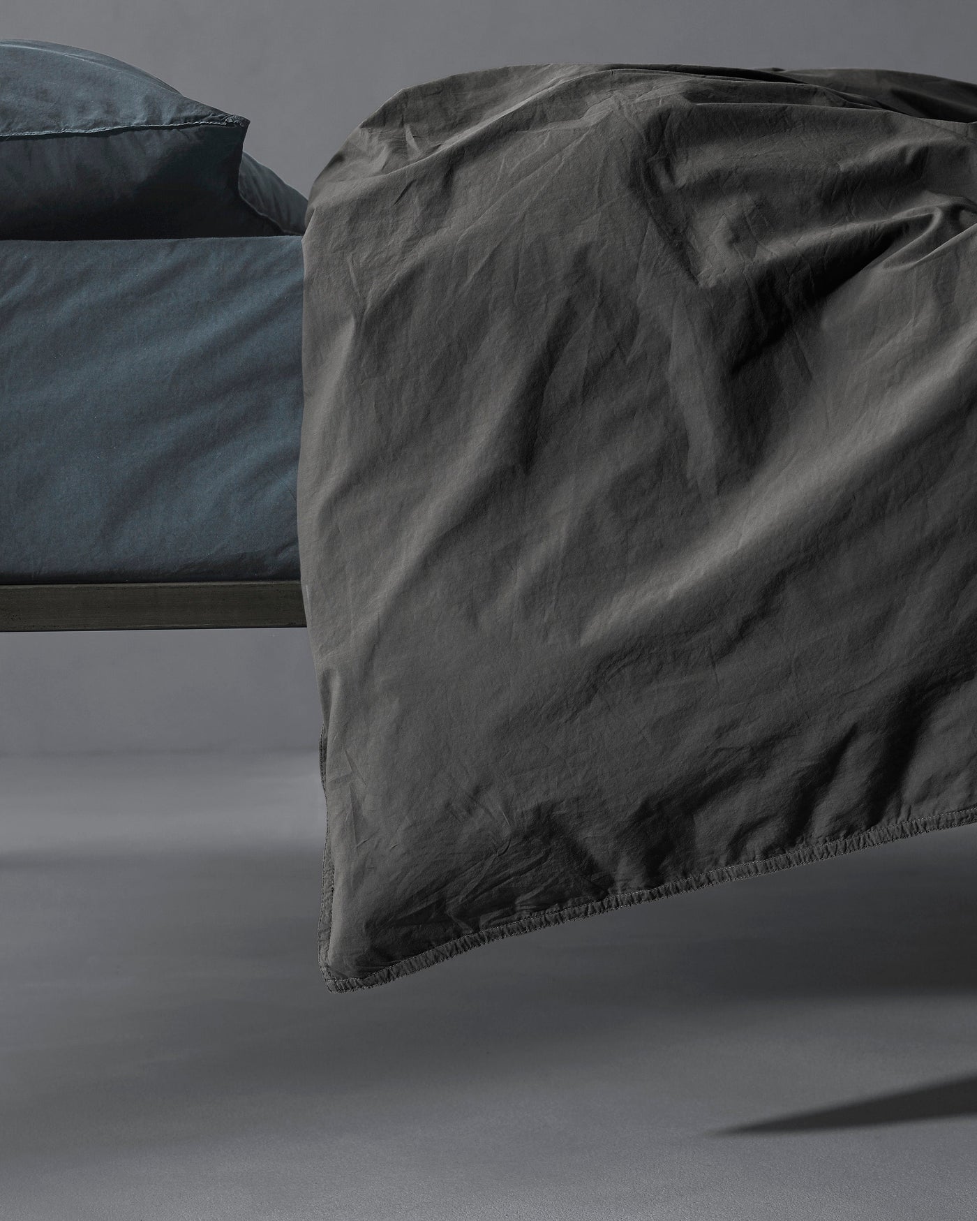 Charcoal washed linen duvet cover draped over bed edge, showing relaxed texture and natural creasing.