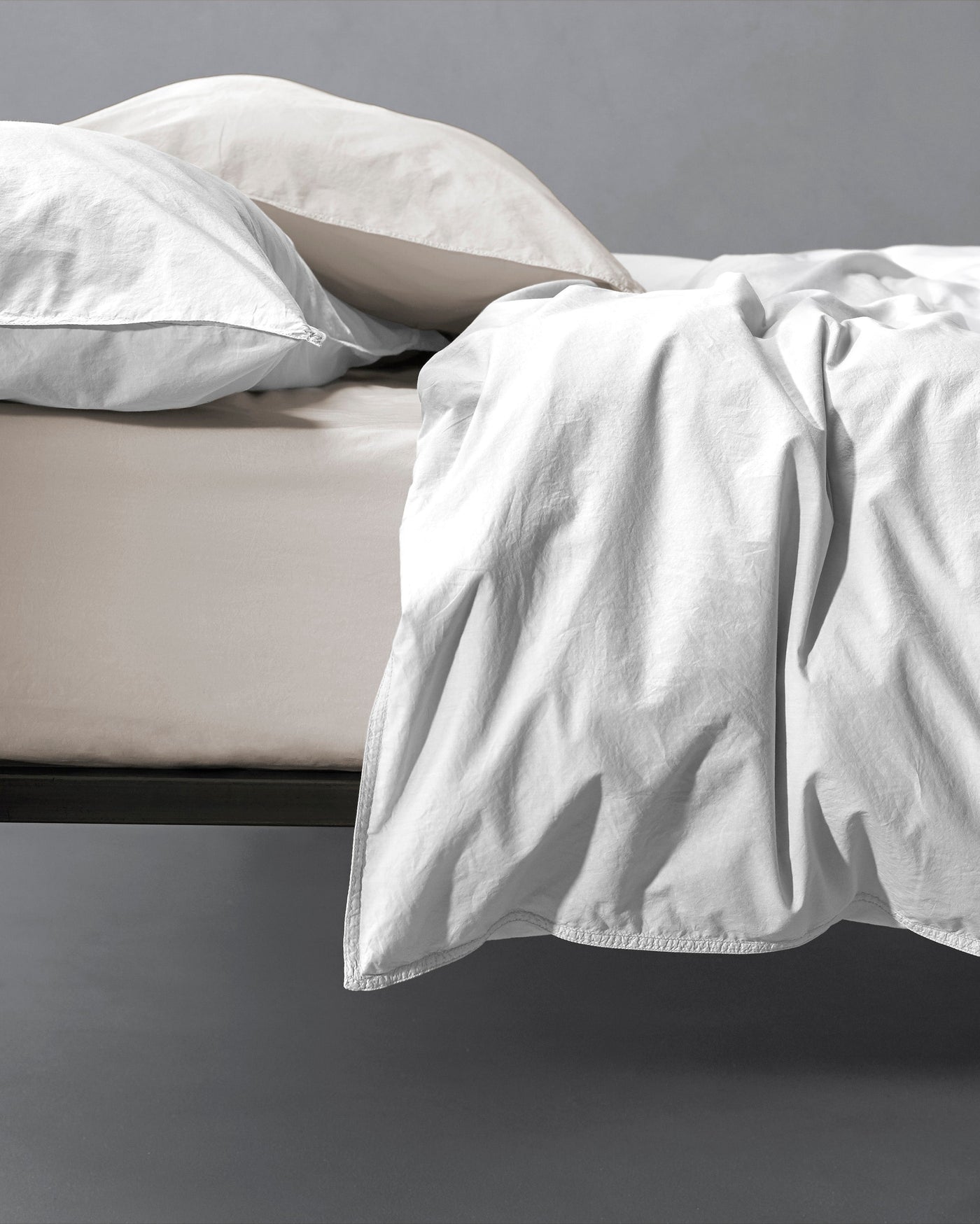 White linen duvet cover draped over foot of bed, showing relaxed texture against stone fitted sheet.