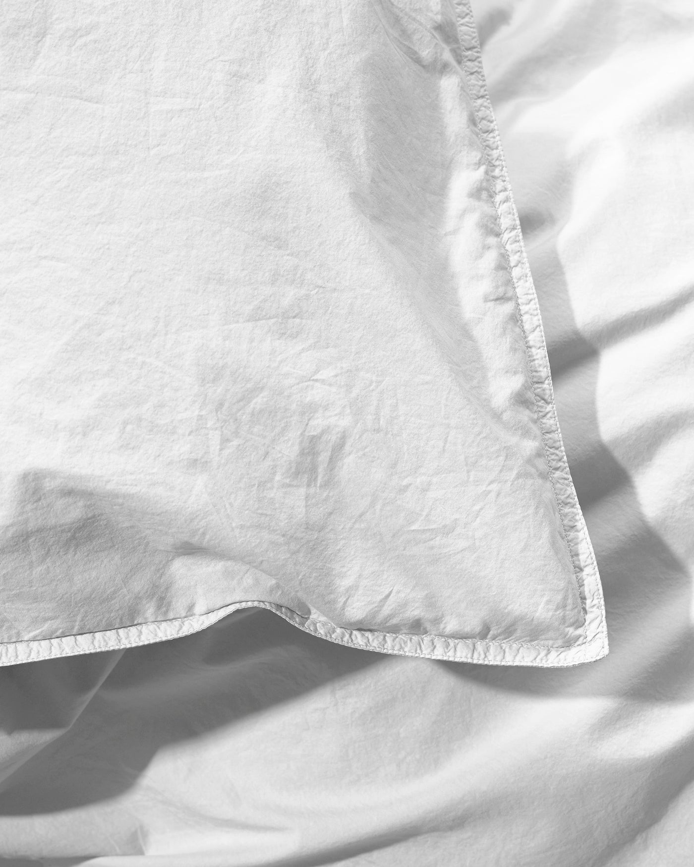 Close-up of white washed cotton duvet cover corner with topstitched hem detail.
