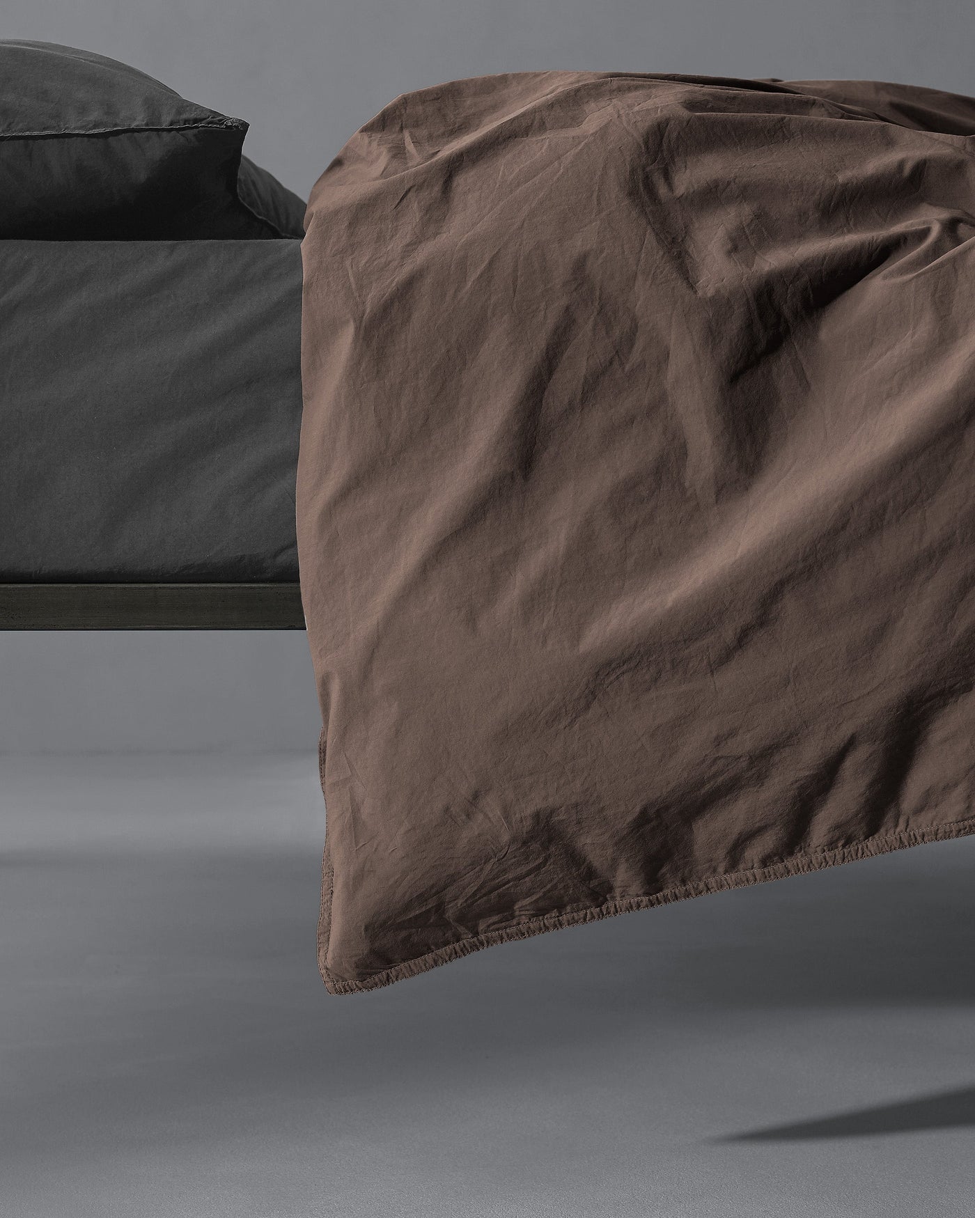 Society Limonta Nite duvet cover in mocha, draped over bed edge showing relaxed linen texture.