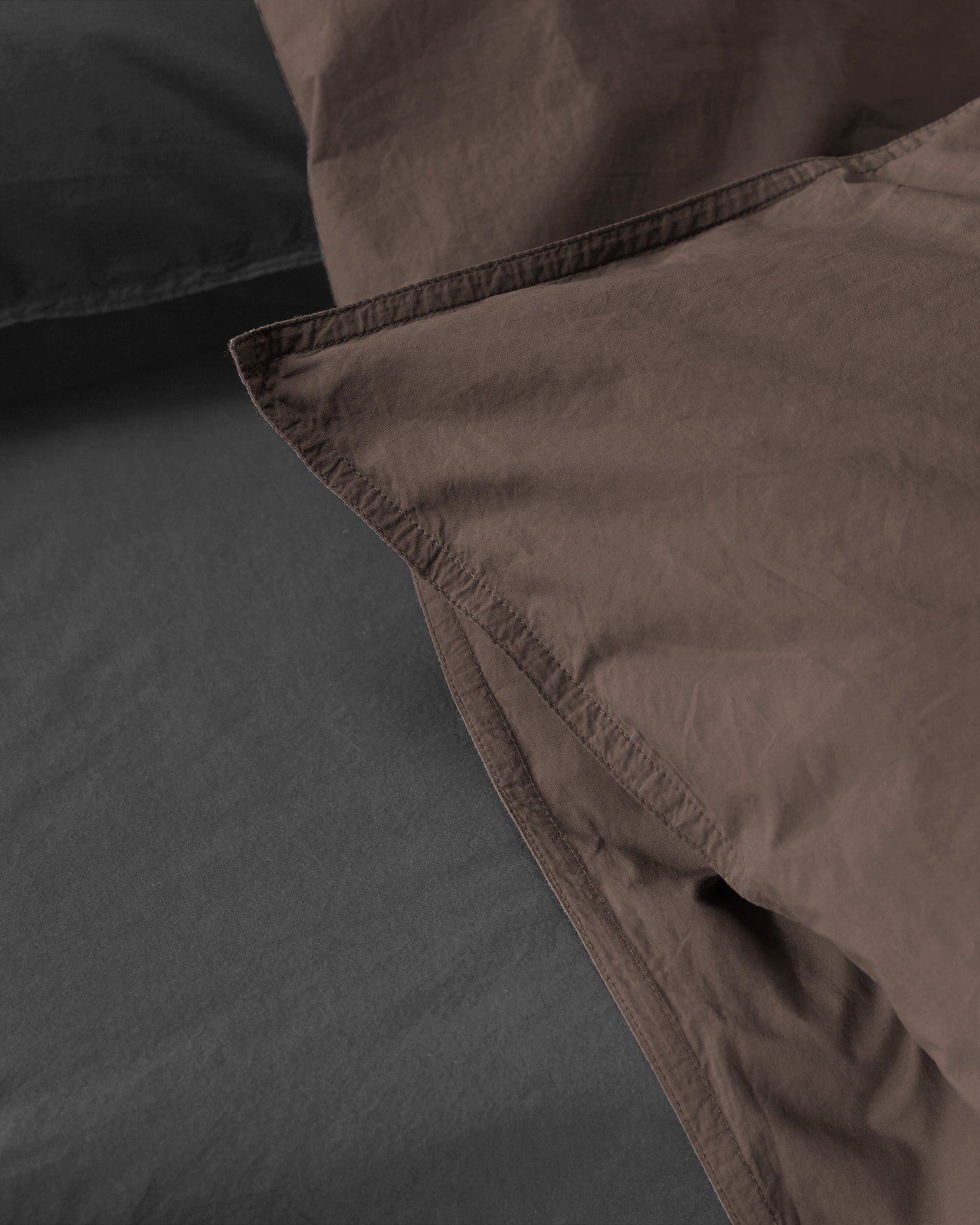 Close-up of folded mocha duvet cover edge against charcoal bedding, showing contrast lining detail.