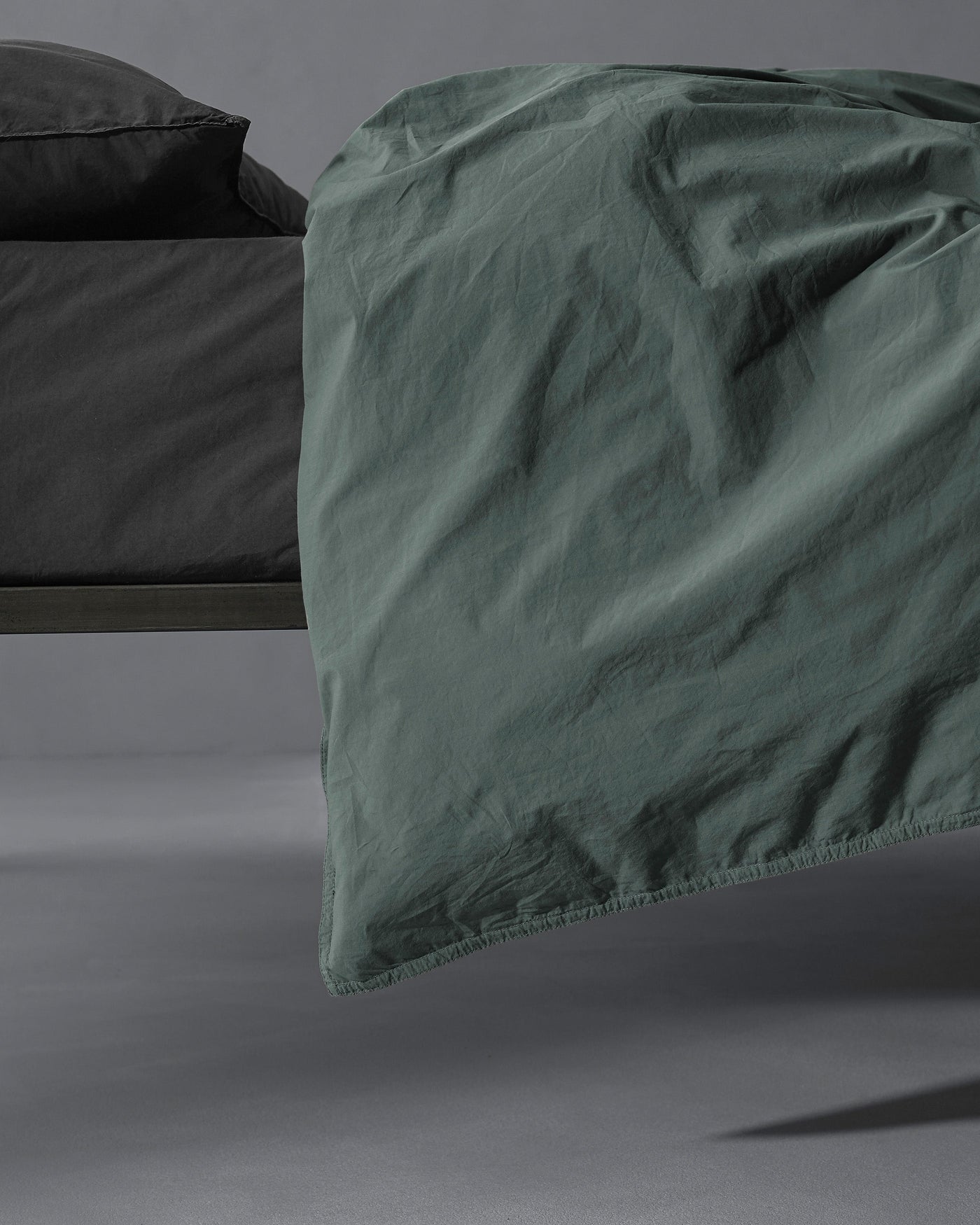 Sage green duvet cover draped over bed edge, showing relaxed linen texture and stitched hem detail.