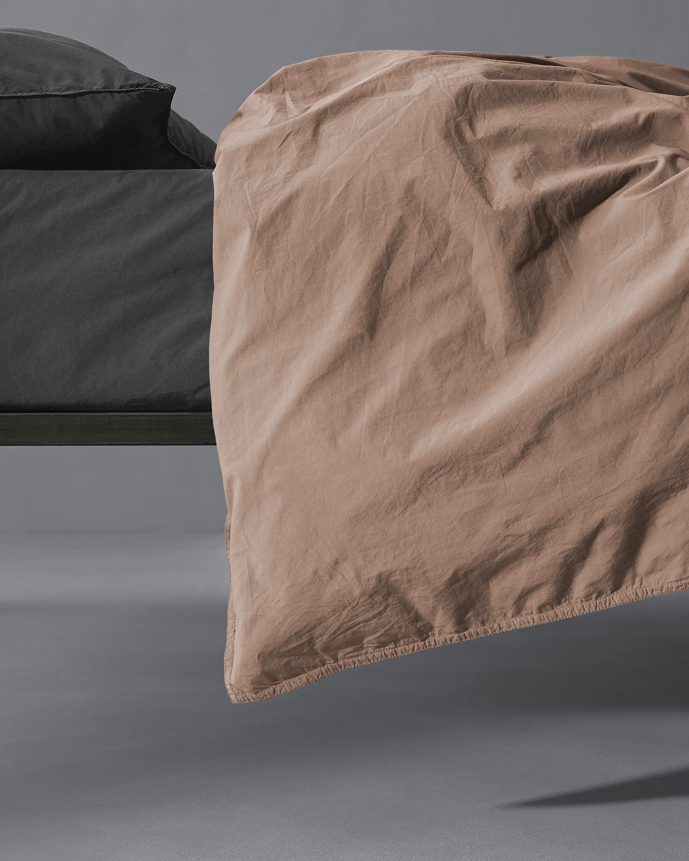 Society Limonta Nite duvet cover in warm taupe, draped over bed edge showing relaxed texture.